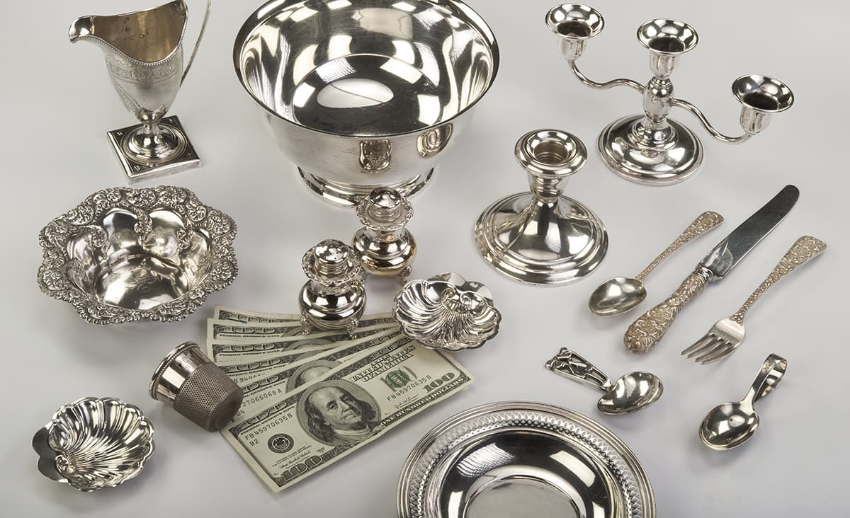 Sterling silver bowl, pitcher, candelabra and flatware beside hundred-dollar bills.