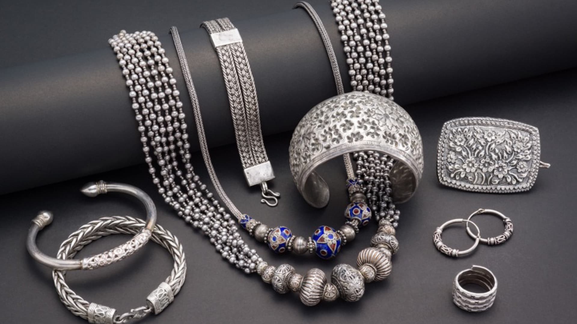 Ornate sterling silver necklaces, filigree cuff and bangles on a dark surface.