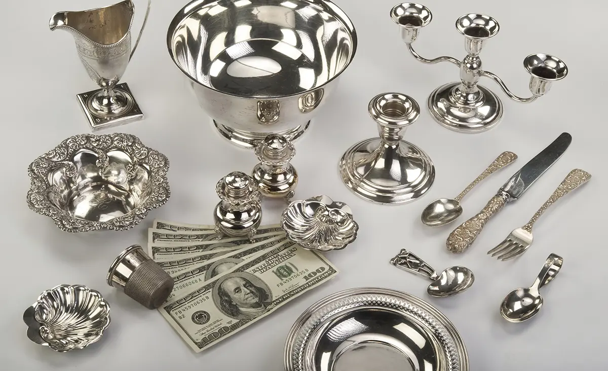 Sterling silver bowl, pitcher, candelabra and flatware beside hundred-dollar bills.